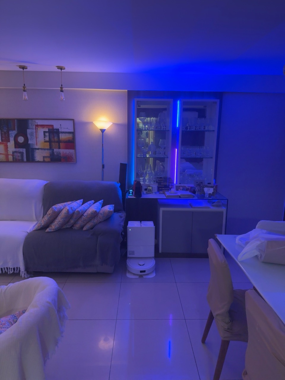 Sala com iluminação azul junto à cristaleira e robô aspirador na base.